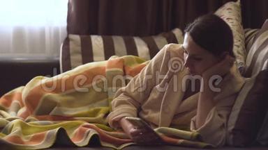 女士穿着米色浴袍，床上有智能手机。